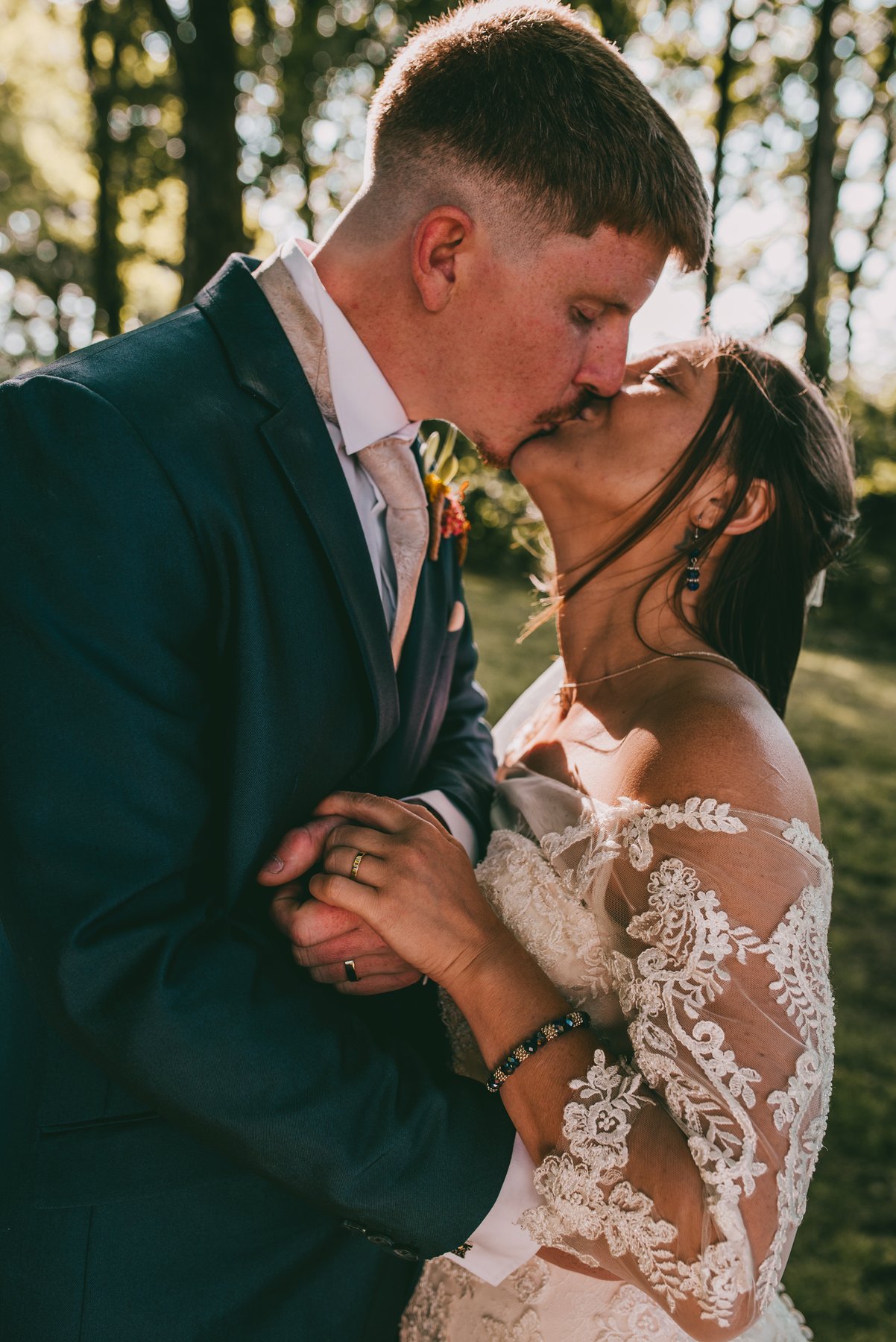 A bride and groom kissing in dappled woodland light